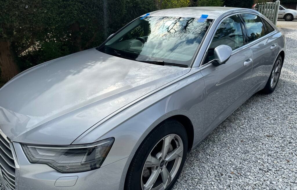 Silver Audi car with a cracked windshield, marked with blue tape for repair