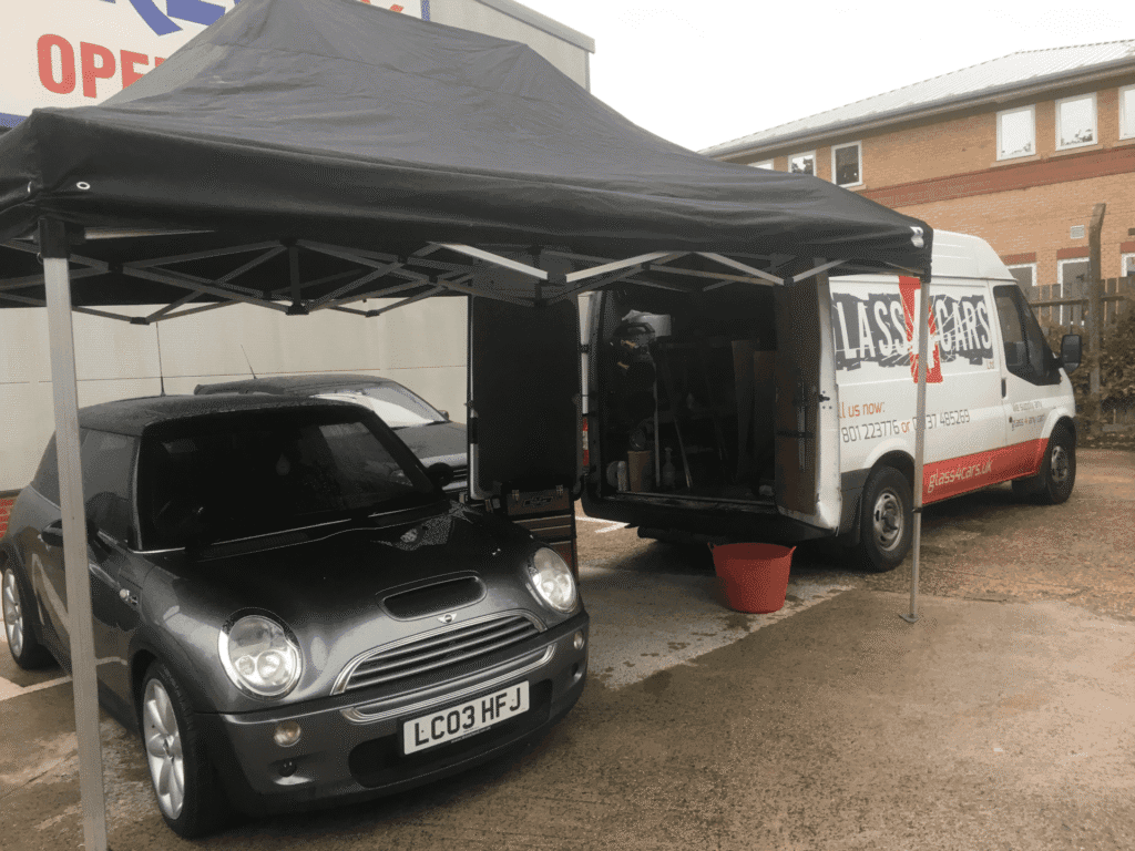 Mobile windscreen repair van set up with canopy while servicing a black car at customer location